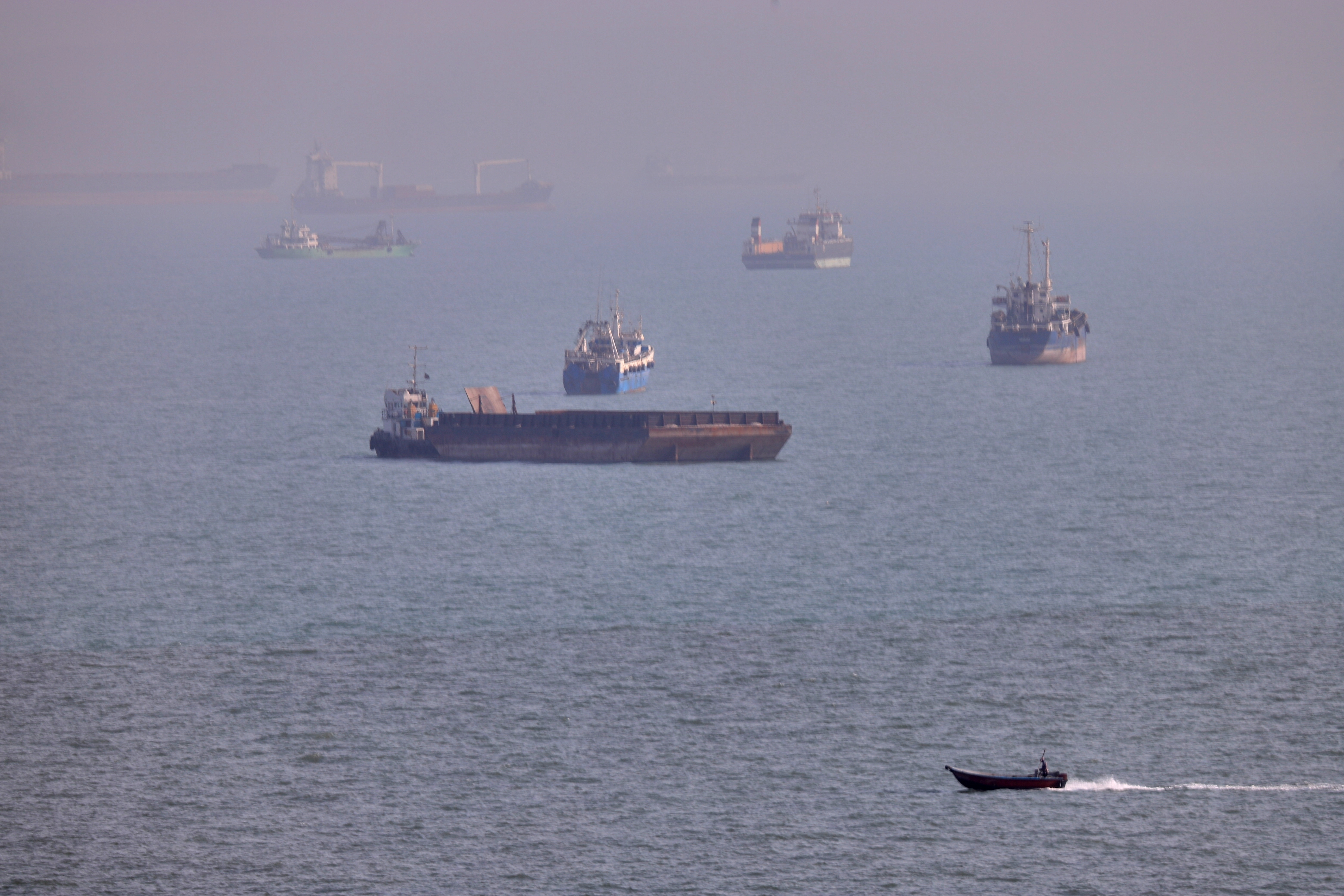 A small boat sails past cargo ships and other commercial vessels anchored in the Strait of Hormuz off Bandar Abbas, Iran, on Aug. 5.